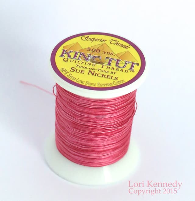 A spool of pink thread on a white surface